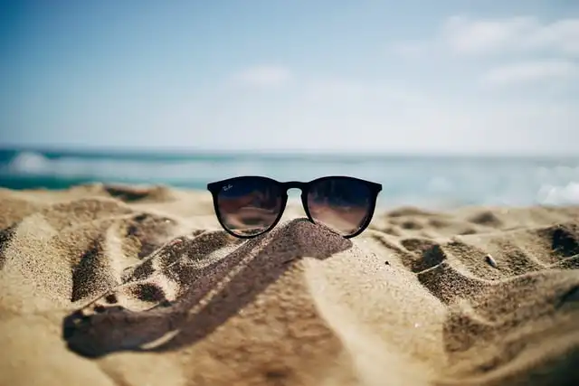 Strandbild mit kleinen Sandhügeln auf denen eine Damen-Sonnenbrille liegt.